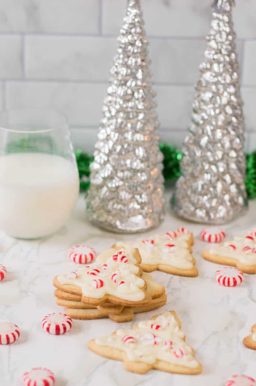 stack of peppermint sugar cookies with milk and Christmas trees in the background