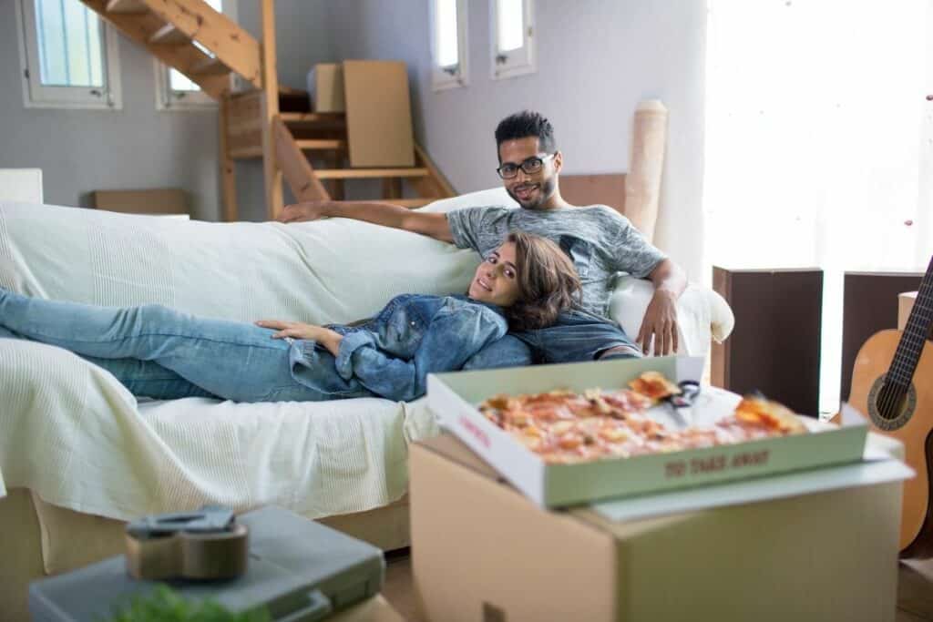 couple watching tv on a couch with a pizza in front of them