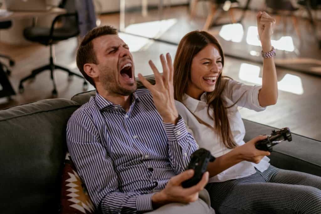 couple playing video games together - man lost and woman is laughing celebrating
