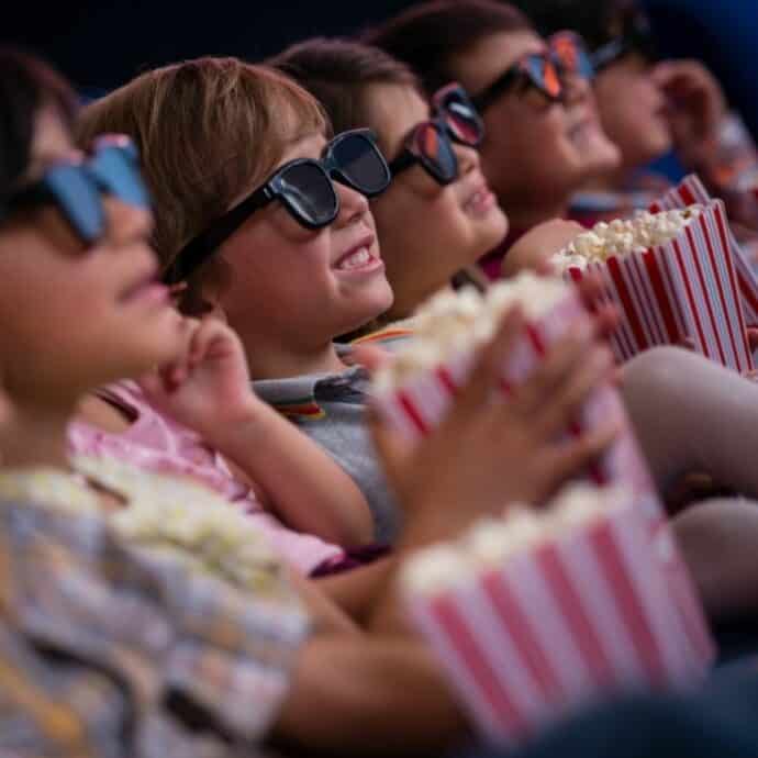 4 kids watching a movie with 3D glasses on and eating popcorn