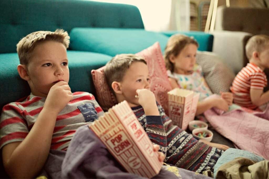 4 kids on the couch watching a movie eating popcorn