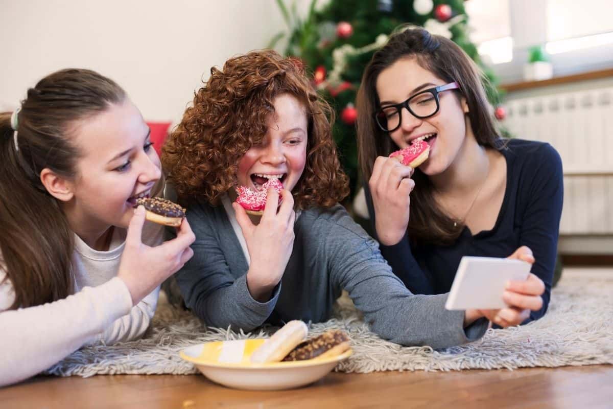 3 girls eating donuts watching one their phones