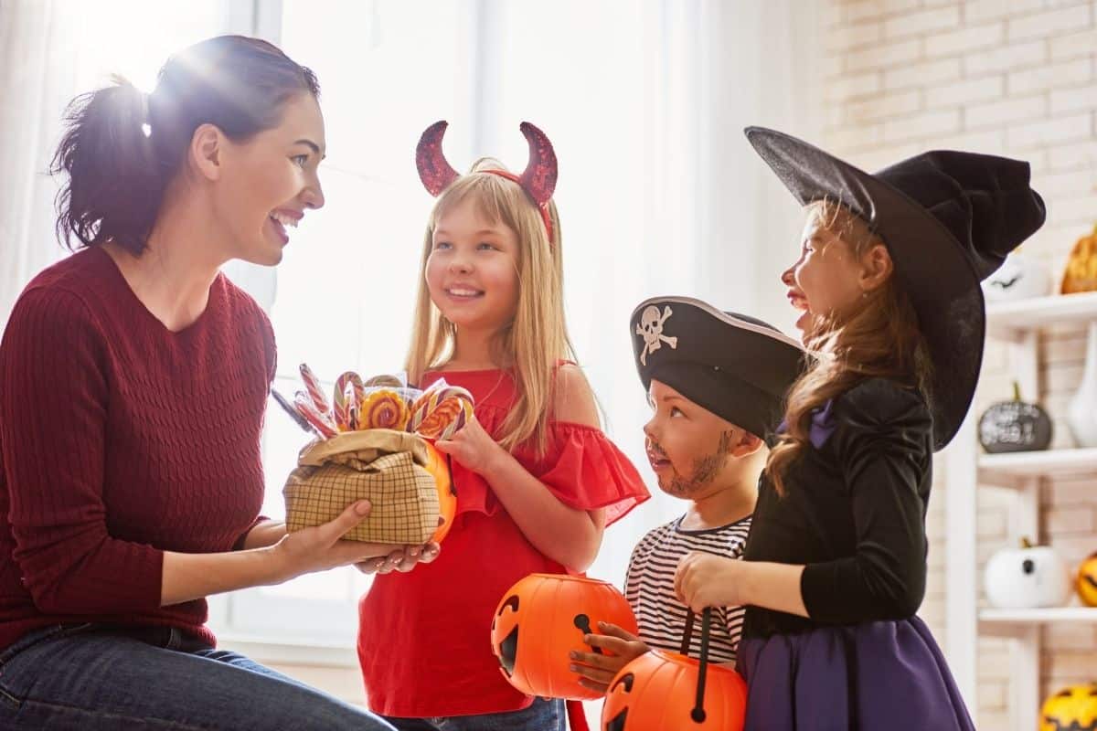 woman giving 3 kids candy inside on halloween