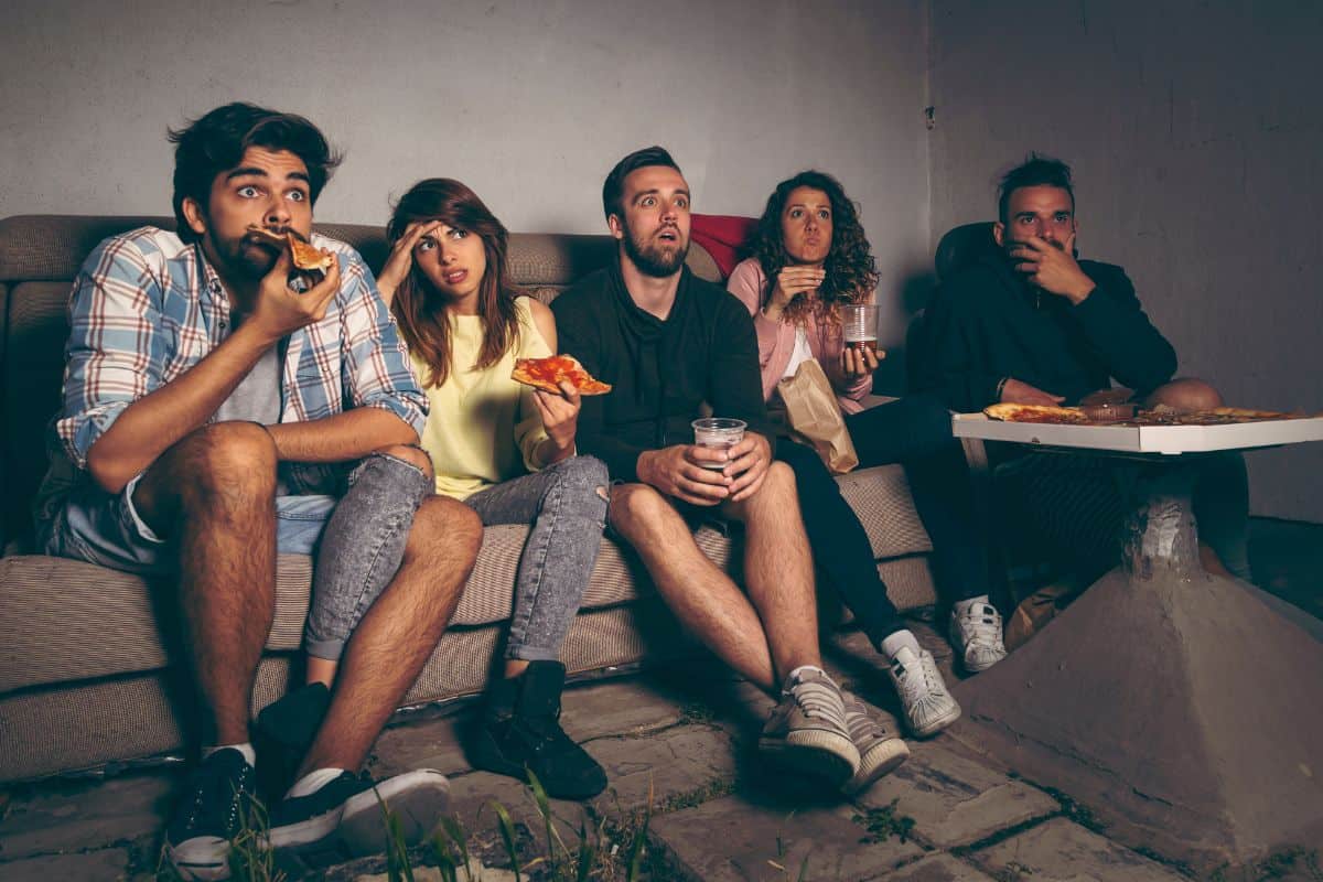  teens watching a movie inside with pizza