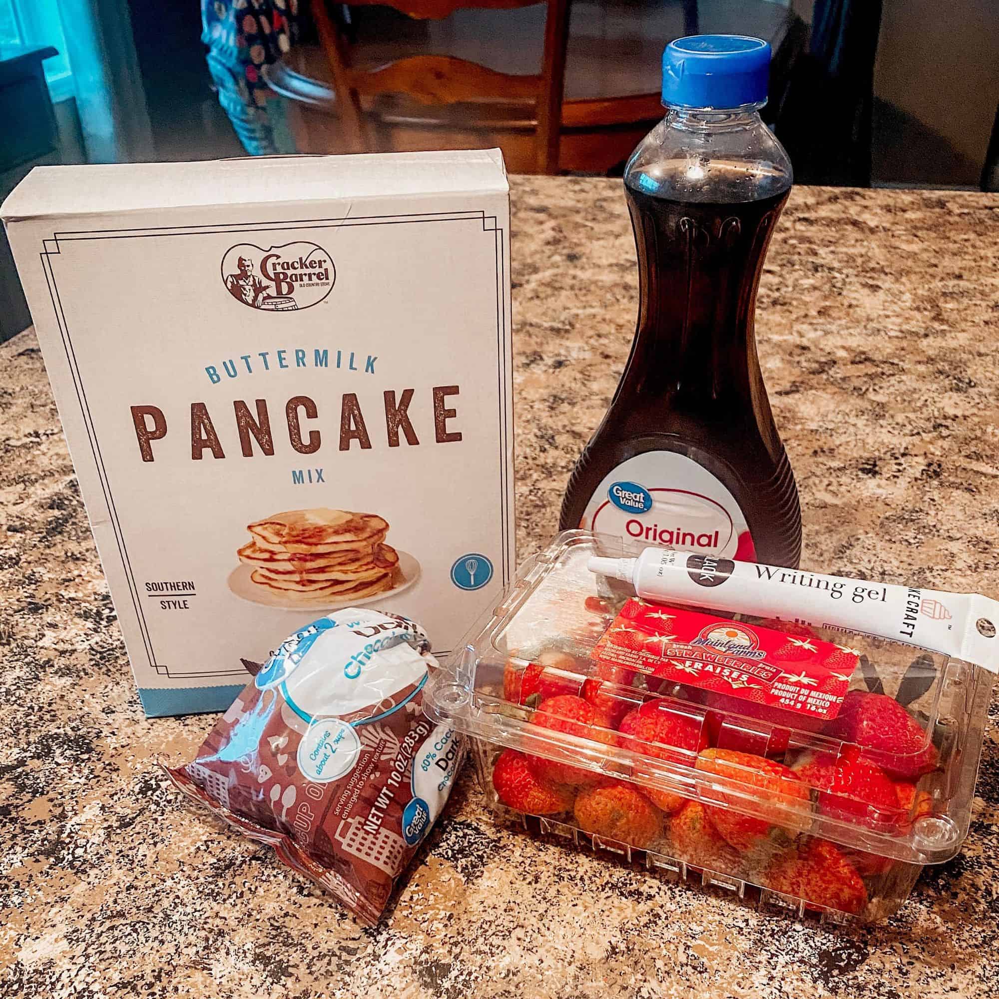 teddy bear pancake ingredients - pancake mix, strawberries, writing gel, chocolate chips and syrup