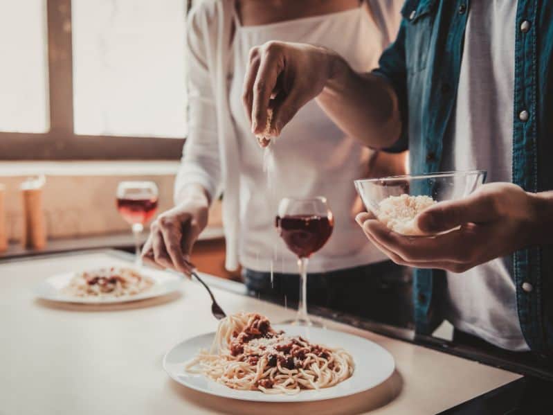 couple topping their homemade spaghetti with cheese